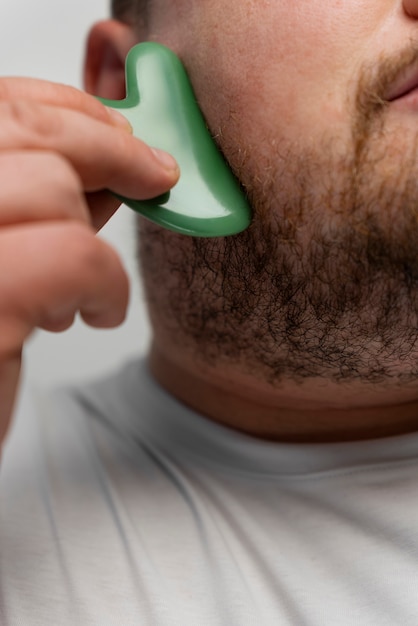 Free photo man using gua sha on his face for skincare