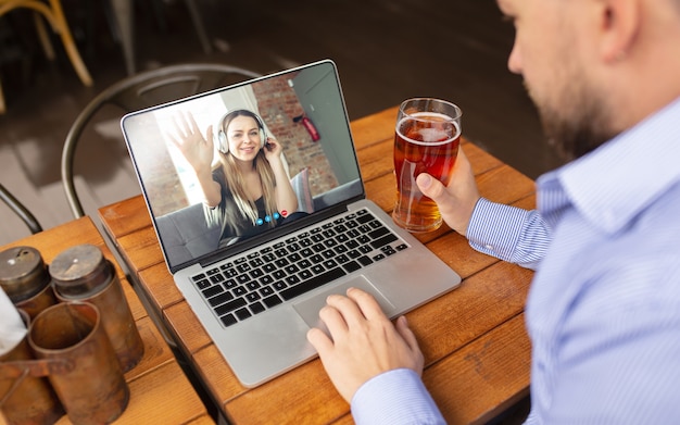 man using laptop for videocall while drinking a beer