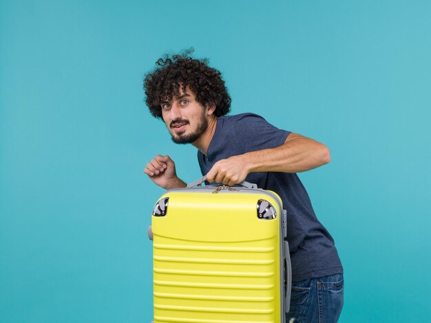 man in vacation in blue t-shirt quietly leaving with his suitcase on blue