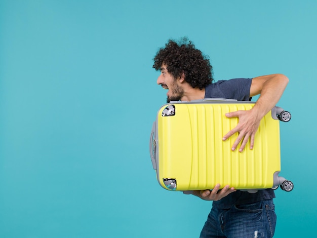 Free Photo man in vacation holding big yellow suitcase on blue