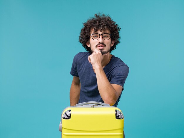 man in vacation with big yellow suitcase on light blue