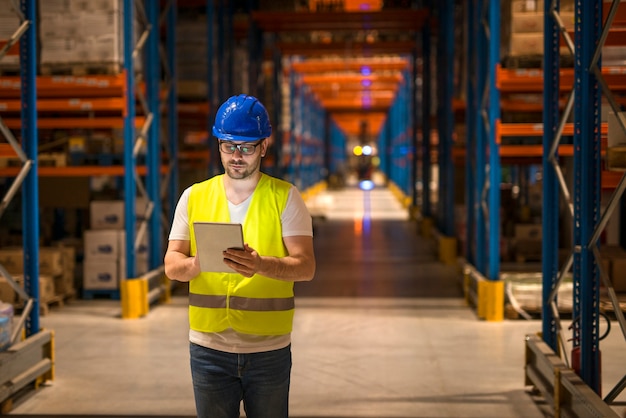 Man walking through large warehouse storage storehouse center and using tablet to control distribution