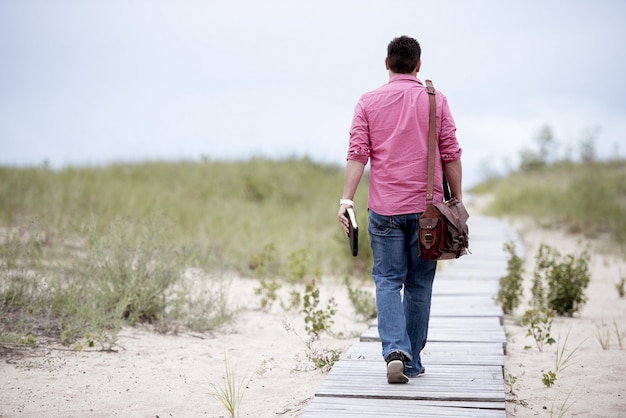 Man walking on a wooden pathway carrying his bag and holding the bible