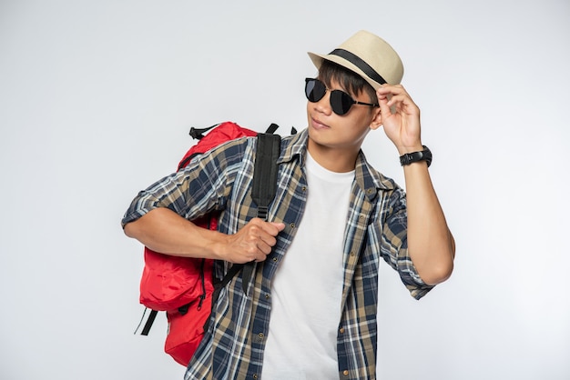 A man wearing glasses goes out to travel, wear a hat and carry a backpack