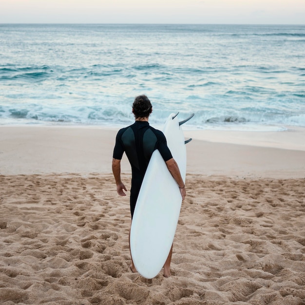 Man wearing surfer clothes walking on the sand from behind