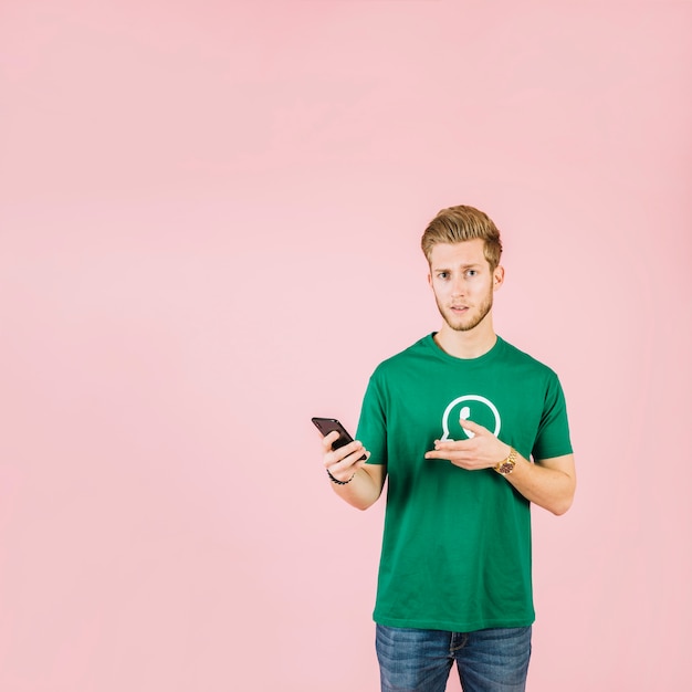 Free Photo man wearing whatsapp icon t-shirt gesturing while holding mobile phone