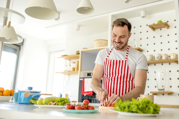 Free Photo man wearing a white apron with red lines and cooking something in the kitchen