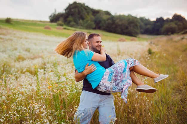 Man whirls blonde woman on the arms standing on the field 