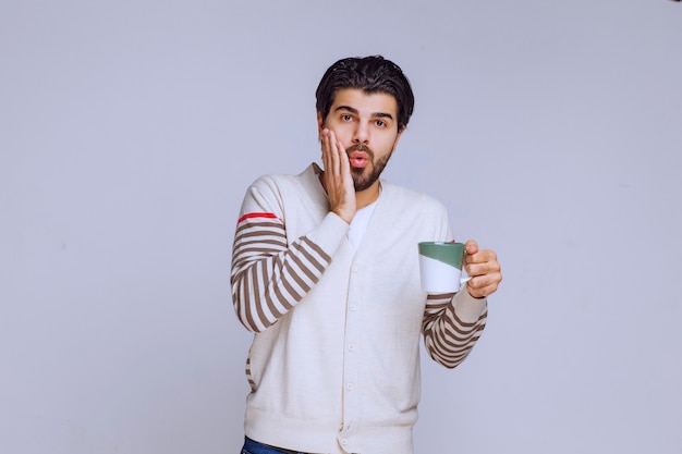 Man in white shirt holding a coffee mug and looks surprized. 