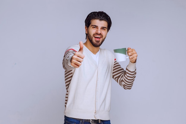 Man in white shirt holding a coffee mug and making good hand sign. 