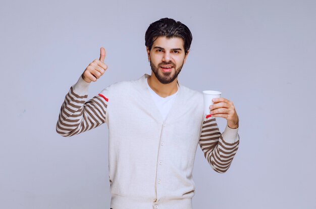 Man in white shirt holding a coffee mug and making good hand sign. 