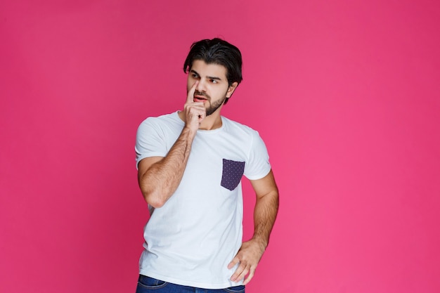 Man in white shirt putting his hand to his face and thinking.