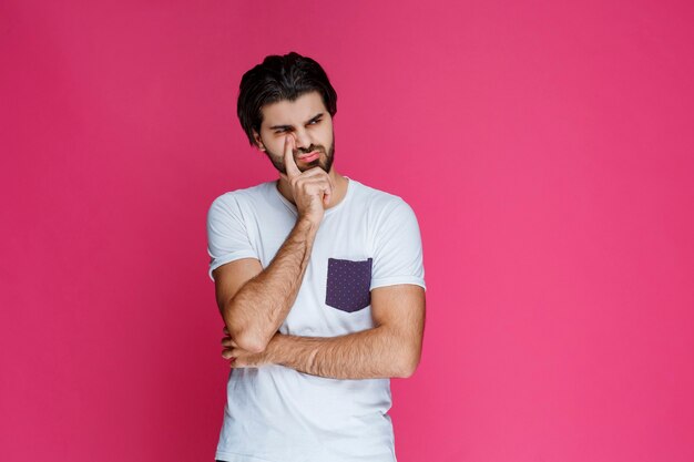 Man in white shirt putting his hand to his face and thinking.