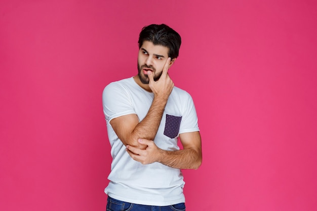 Man in white shirt putting his hand to his face and thinking.