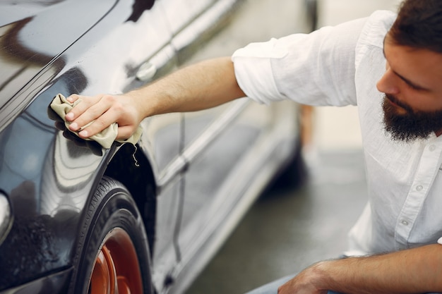 Man in a white shirt wipes a car in a car wash