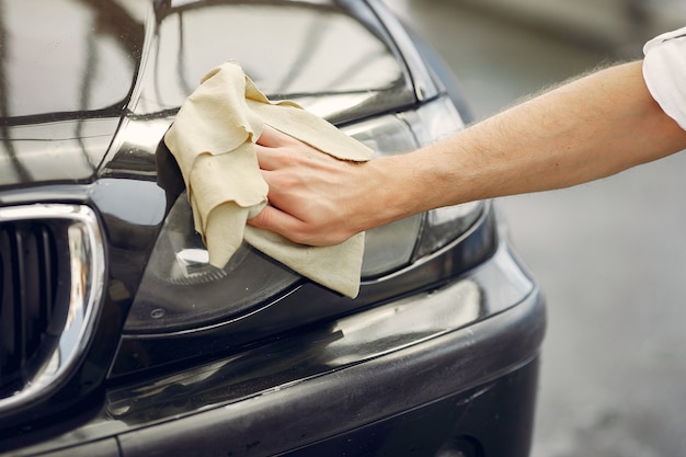 Man in a white shirt wipes a car in a car wash