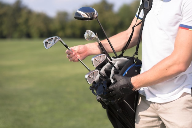 Free photo man in white tshirt removing a golf club from his golf bag to start playing