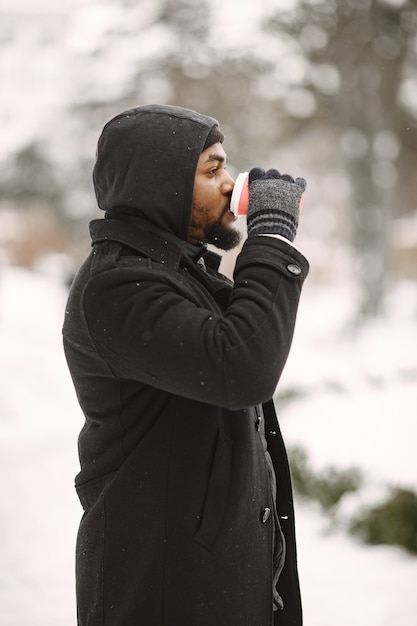 Free Photo man in a winter town. guy in a black coat. man with coffee.