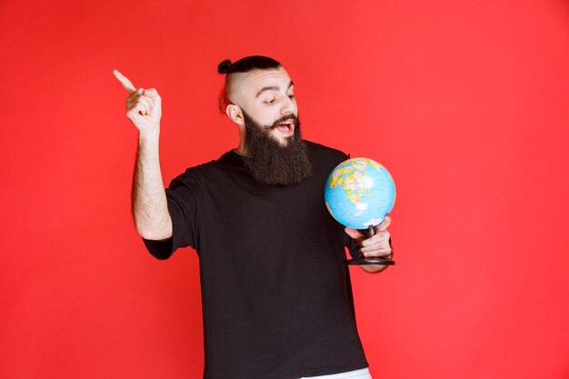 Man with beard holding a globe and pointing to somewhere.