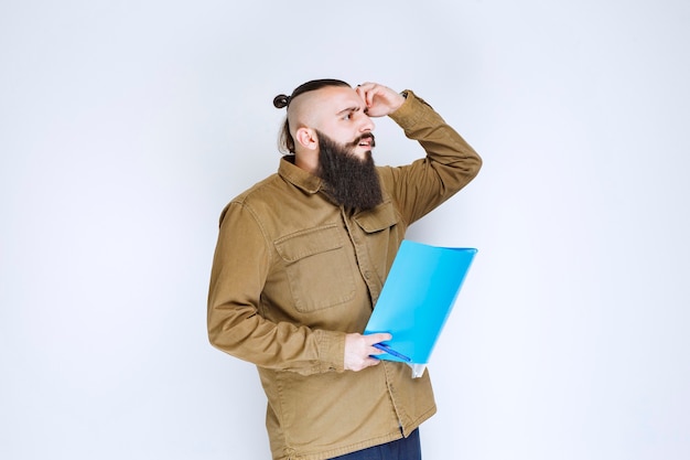 Free photo man with beard holding a quiz paper and looks confused and thoughtful.