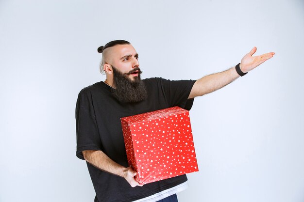 Man with beard holding a red gift box and arguing with someone.  