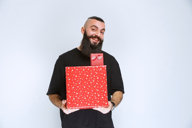 Man with beard holding red gift boxes and offering it to his girlfriend.