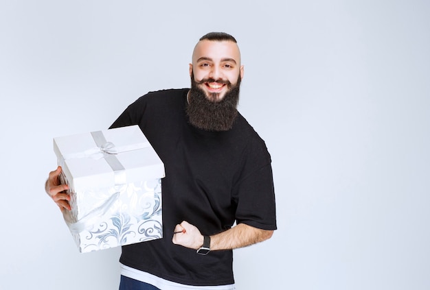 Free photo man with beard holding a white blue gift box and feeling successful.