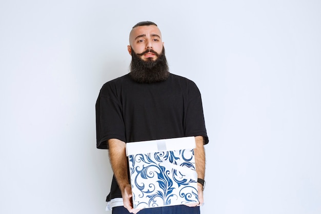 Free Photo man with beard holding a white blue gift box and looks disappointed. 