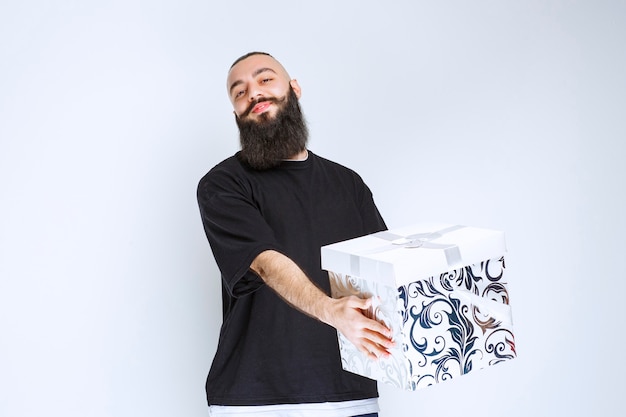 Free photo man with beard holding a white blue gift box smiling and feeling happy.