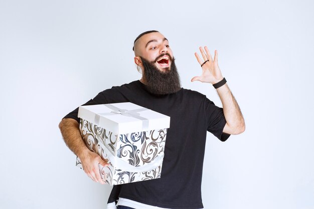 Free photo man with beard holding a white blue gift box smiling and feeling happy.