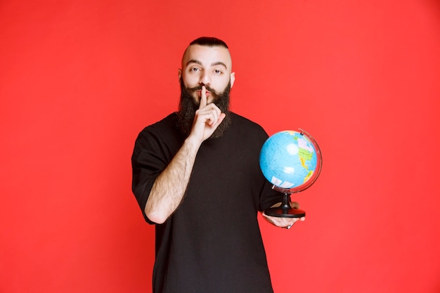 Man with beard holding a world globe and asking for silence.