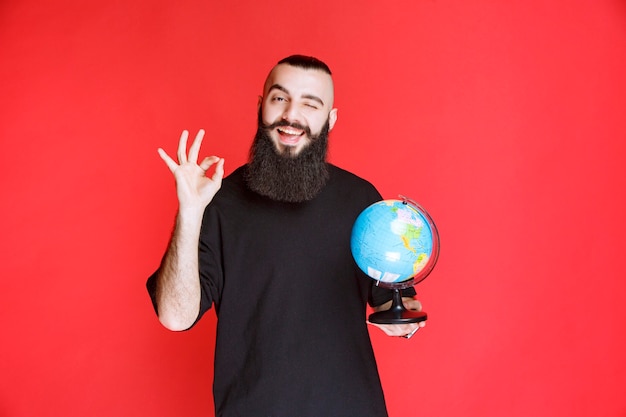 Free photo man with beard holding a world globe and enjoying it.