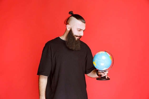 Free Photo man with beard holding a world globe and looking for places over it.