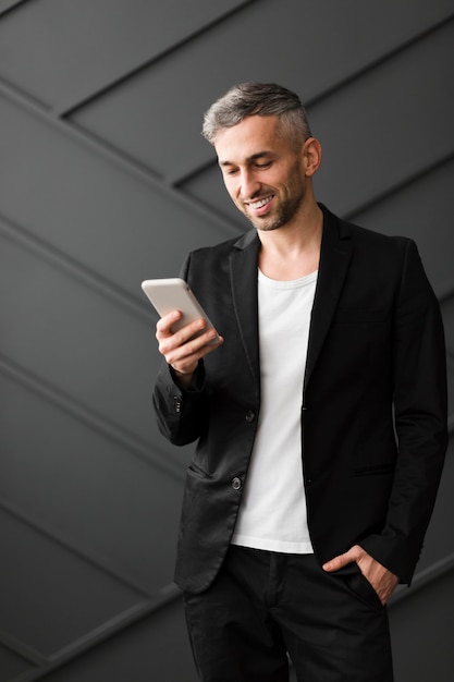 Man with black jacket smiling at his mobile phone