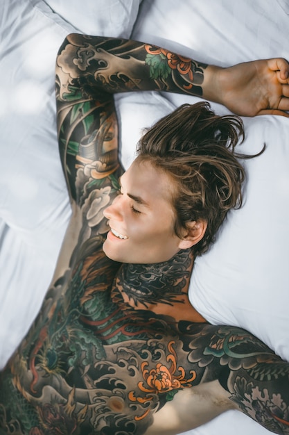 Man with colorful tattoos posing on a white sheet