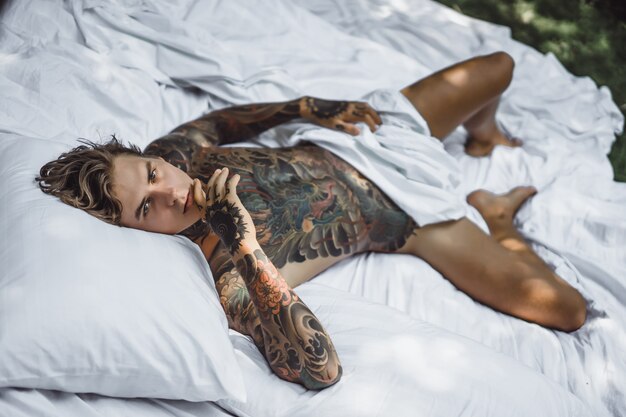 Man with colorful tattoos posing on a white sheet