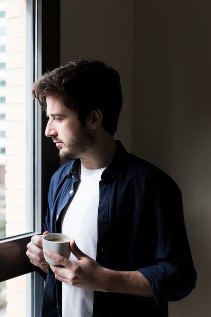 Man with drink looking out office window