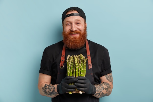 Free photo man with ginger beard in apron and gloves holding asparagus