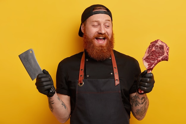 Free photo man with ginger beard in apron and gloves holding meat and knife