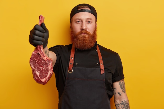 Free photo man with ginger beard in apron and gloves holding meat