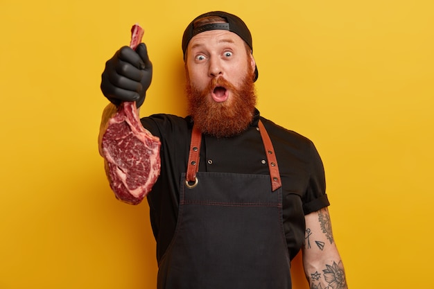 Man with ginger beard in apron and gloves holding meat