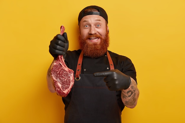 Man with ginger beard in apron and gloves holding meat