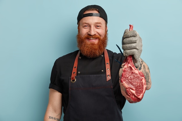 Free photo man with ginger beard in apron and gloves holding meat