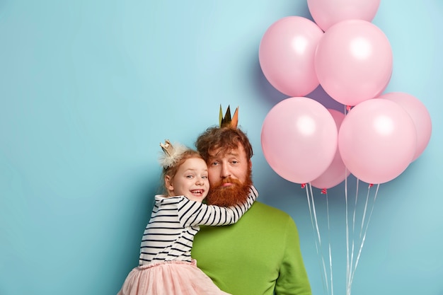 Free photo man with ginger beard and his daughter with party accessories