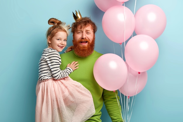 Man with ginger beard and his daughter with party accessories