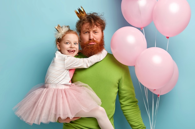 Free photo man with ginger beard and his daughter with party accessories