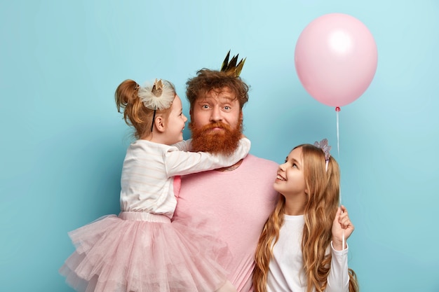 Free photo man with ginger beard and his daughters with party accessories