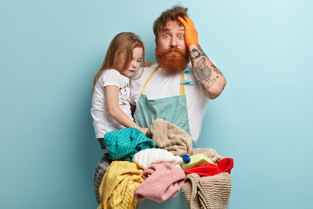 Man with ginger beard holding his daughter and doing laundry