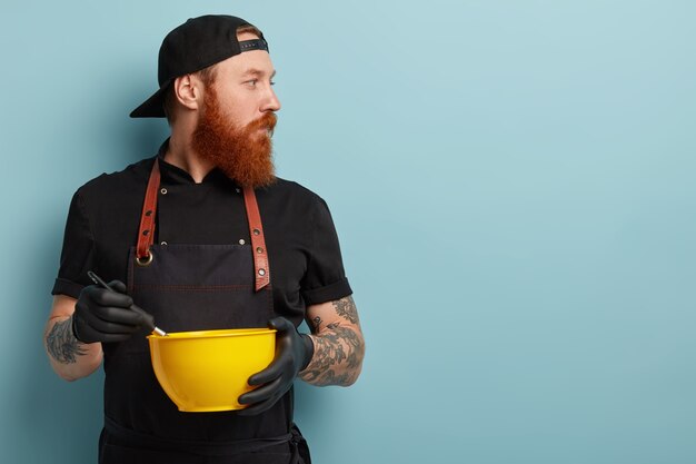 Man with ginger beard wearing apron and gloves holding bowl