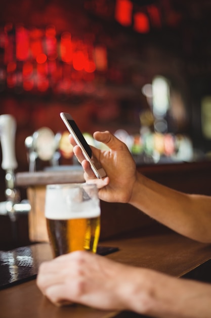 Man with glass of beer using mobile phone in counter